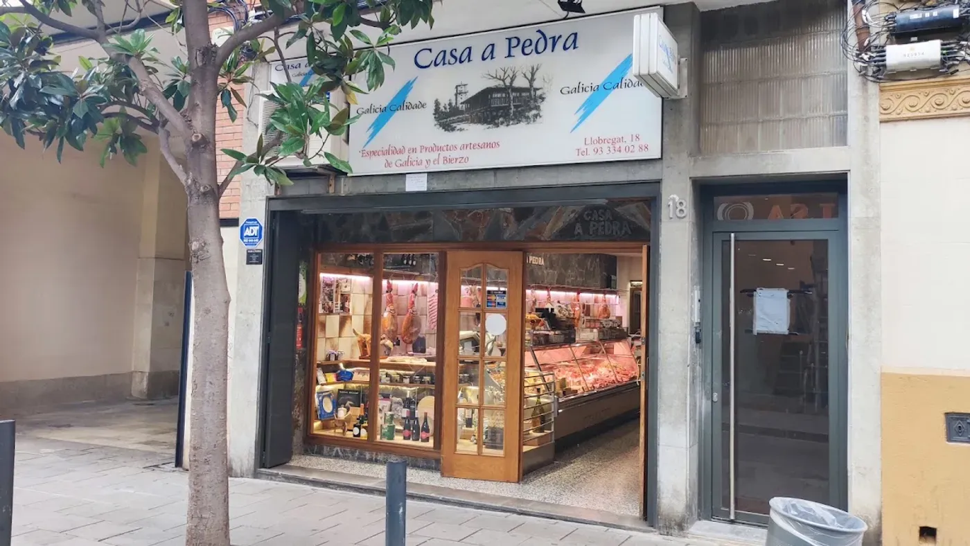 Fachada de Casa a Pedra en Carrer Llobregat 18, con el rótulo azul y los rayos de la bandera gallega